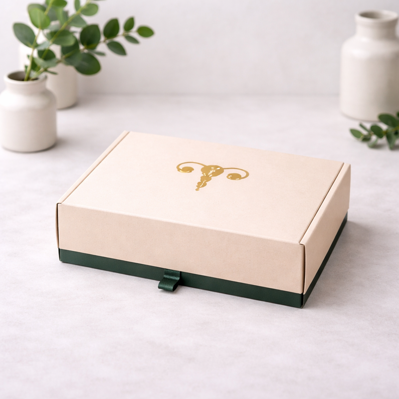 Beige gift box with a gold emblem on a light surface with decorative vases and plants.
